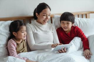 mother and two kids in bed looking at computer screen