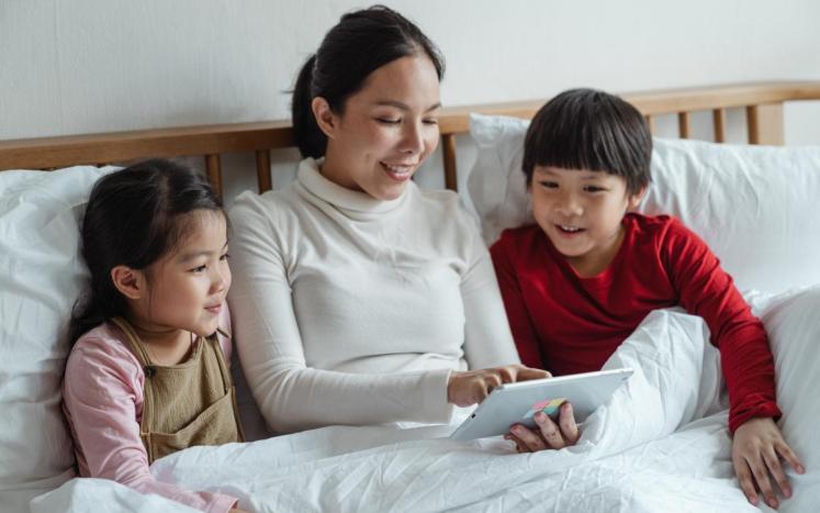 mother and two kids in bed looking at computer screen